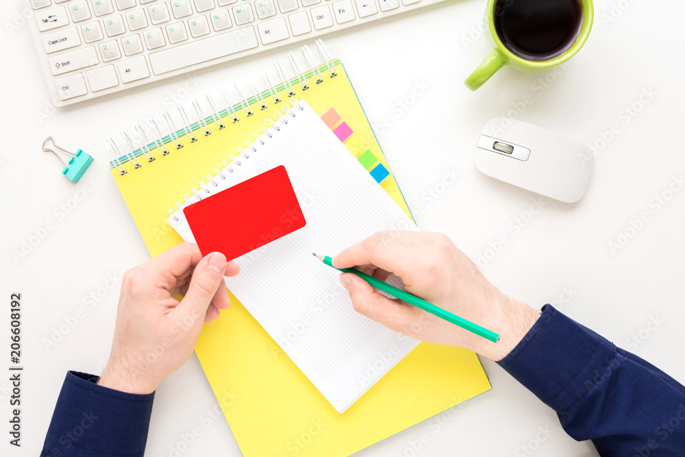 white Desk, guy writes in a notebook, holding a business card, pensil, notebook, white background with copy space, for advertisement, top view white Desk, guy writes in a notebook, holding a business card, pensil, notebook, white background with copy space, for advertisement, top view