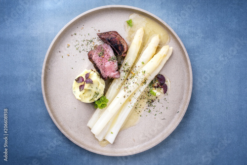 Modern barbecue dry aged sliced fillet steak with white asparagus in butter sauce and mashed potatoes as top view on a plate with copy space