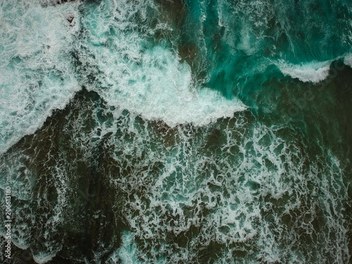 Aerial view of ocean waves and brown rocks in the coastline