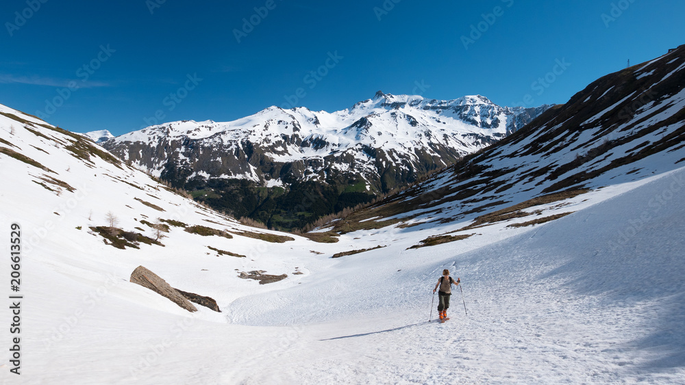 Alpinist hiking ski touring on snowy slope towards the mountain summit. Concept of conquering adversities and reaching the goal.