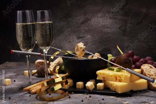 Fototapeta Naklejka Na Ścianę i Meble -  Gourmet Swiss fondue dinner on a winter evening with assorted cheeses on a board alongside a heated pot of cheese fondue