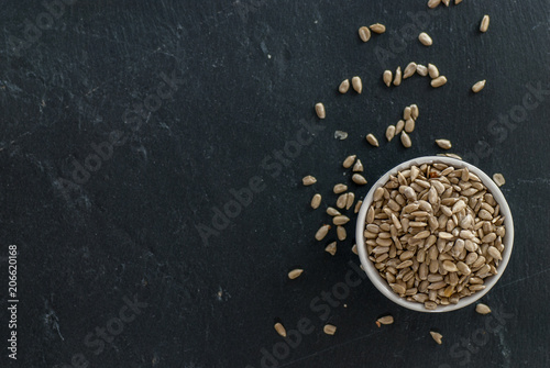 bowl with raw sunflower kernels and kernels spread around on a slate plate with copy space