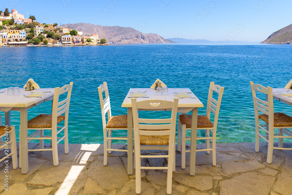 Tables with chairs overlooking sea bay on Symi island in Greece.
