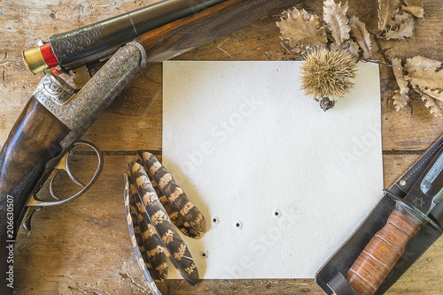 Hunting season concept: beautiful hunting gun with cartridges, knife, paper on old wooden background