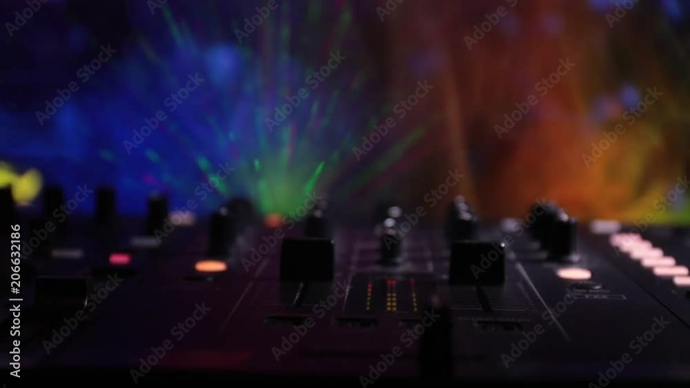 Slider shot. In selective focus of Pro dj controller.The DJ console deejay mixing desk at music party in nightclub with colored disco lights. Close up view