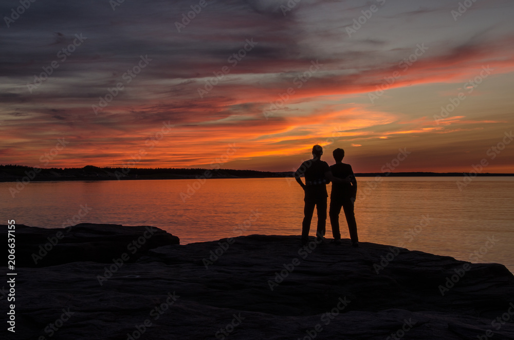 Backlit Couple on large rock overlooking colorful maritime sunset