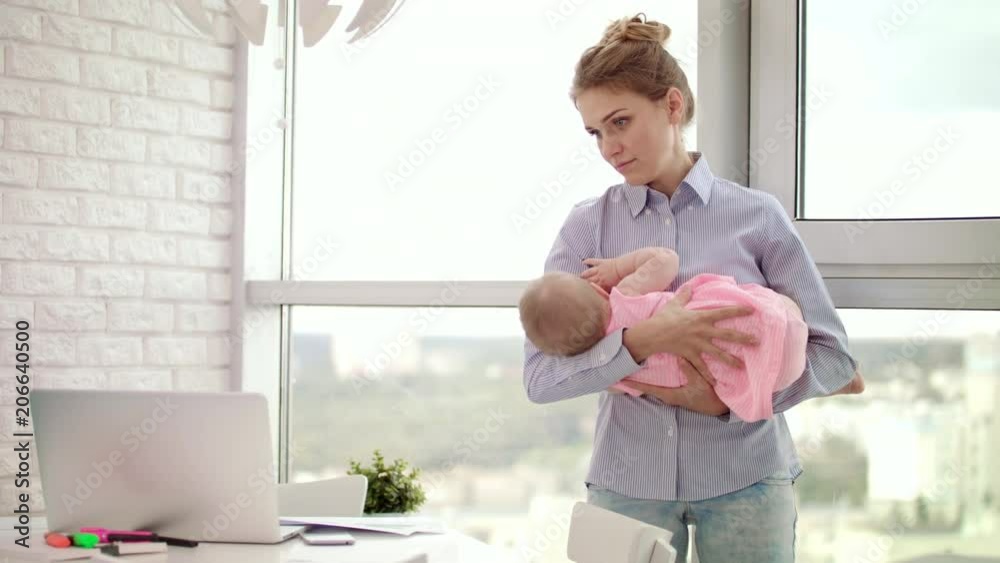 Mom holding baby on hands at workplace in office. Little girl sleeping on mother hands at work. Business woman embracing child at working space. Sleeping infant in mother embrace. Modern motherhood Mom holding baby on hands at workplace in office. Little girl sleeping on mother hands at work. Business woman embracing child at working space. Sleeping infant in mother embrace. Modern motherhood