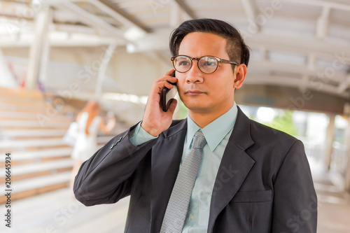 Young Asia handsome businessman with his smartphone standing on walkway of modern city.