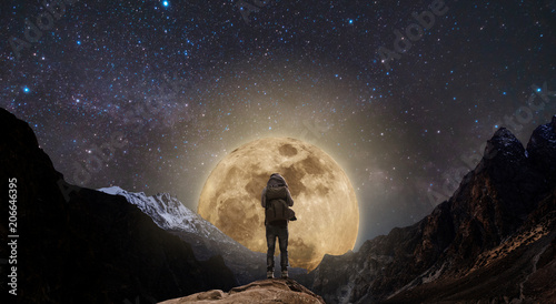 a man standing on mountain peak at night, and full moon on night sky full of stars photo