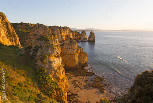 Coastline at sunrise in Algarve Portugal. Secluded empty sandy beach with rocks and nearby cliffs at sunrise.