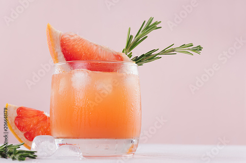 Summer fresh homemade grapefruit lemonade with ice cubes and rosemary closeup on light pink background.