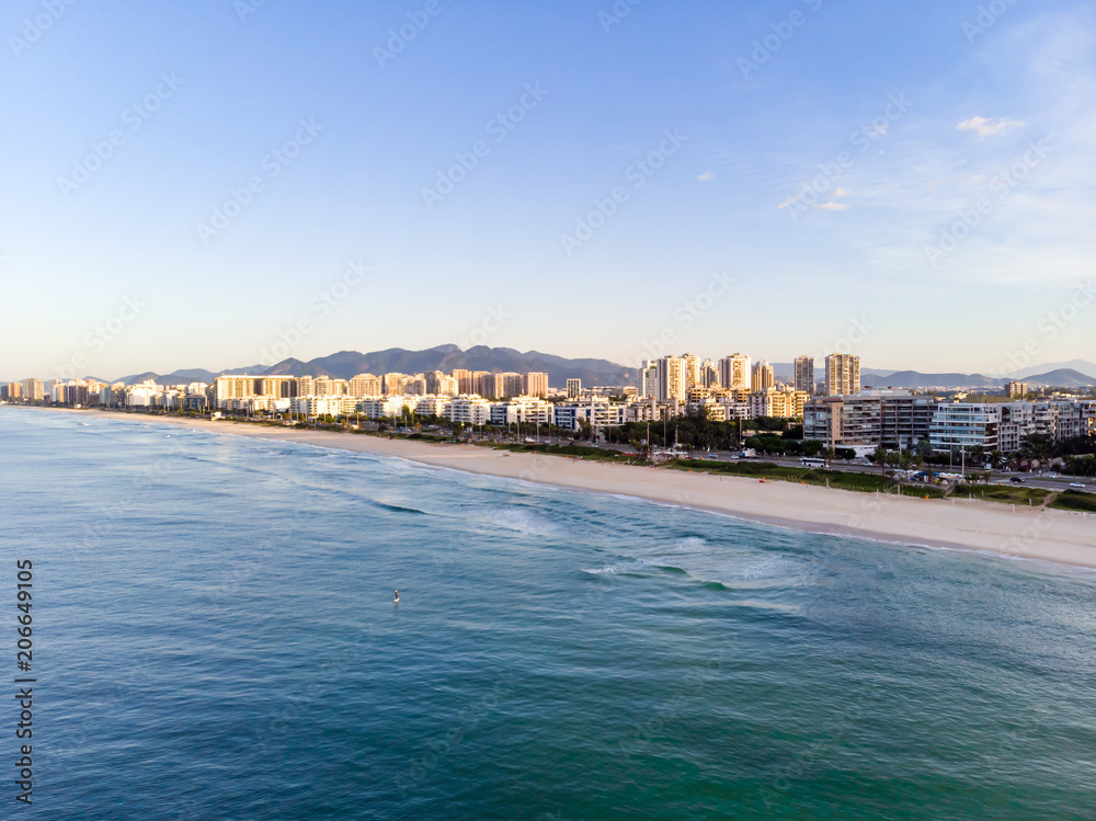 aerial landscape photo of Barra da Tijuca beach , with waves crashing on beach during sunrise, with the beachfront buildings in the background
