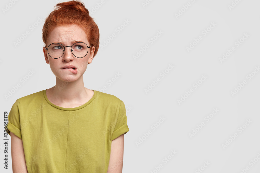 Studio shot of puzzled foxy female has thoughtful expression, curves lips in hesitation, thinks about something with worried look, poses against white background with blank space for yor text Studio shot of puzzled foxy female has thoughtful expression, curves lips in hesitation, thinks about something with worried look, poses against white background with blank space for yor text
