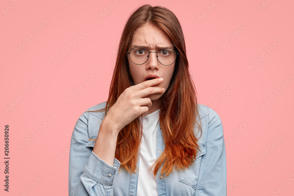 Sad pretty student with gloomy sullen expression, covers mouth with hand, has discontent look as realizes she answered wrong during final test, worries about issue. Unhappy woman says: Oops!