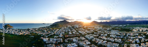 aerial panorama of Recreio dos Bandeirantes beach during sunset, the Pontal Stone on the left, with the sun dipping behind the mountains and causing lens orange lens flare