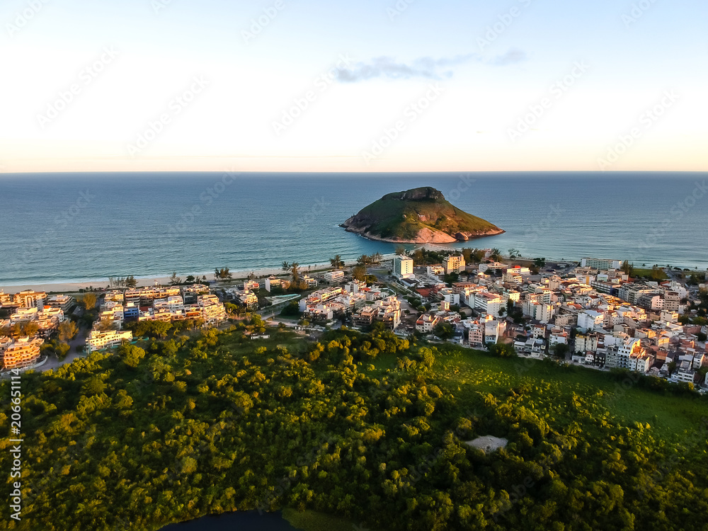 aerial landscape photo of Recreio dos Bandeirantes beach during sunset, with views of Chico Mendes park and the Pontal Stone bathed by orange sunlight