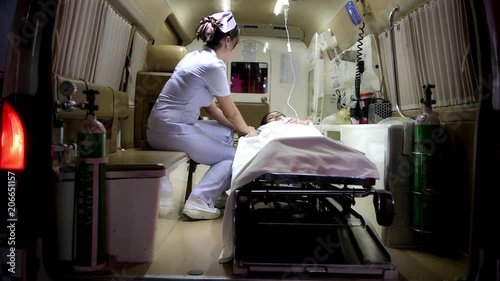 Accident victim inside ambulance at night being treated by nurse. Chinese young female patient laying in bed in ambulance with beautiful female nurse checking her conditions. Sliding dolly shot.