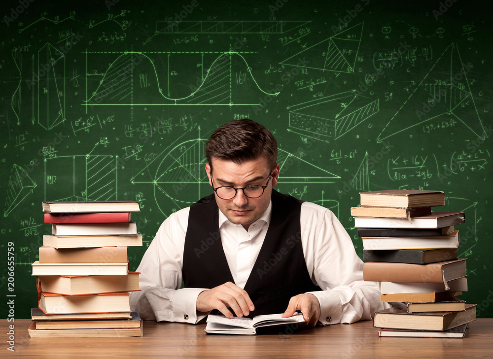 A young passionate male teacher sitting at school desk, reading a book, with area algorythm calculations and numbers on the blackboard concept. A young passionate male teacher sitting at school desk, reading a book, with area algorythm calculations and numbers on the blackboard concept.
