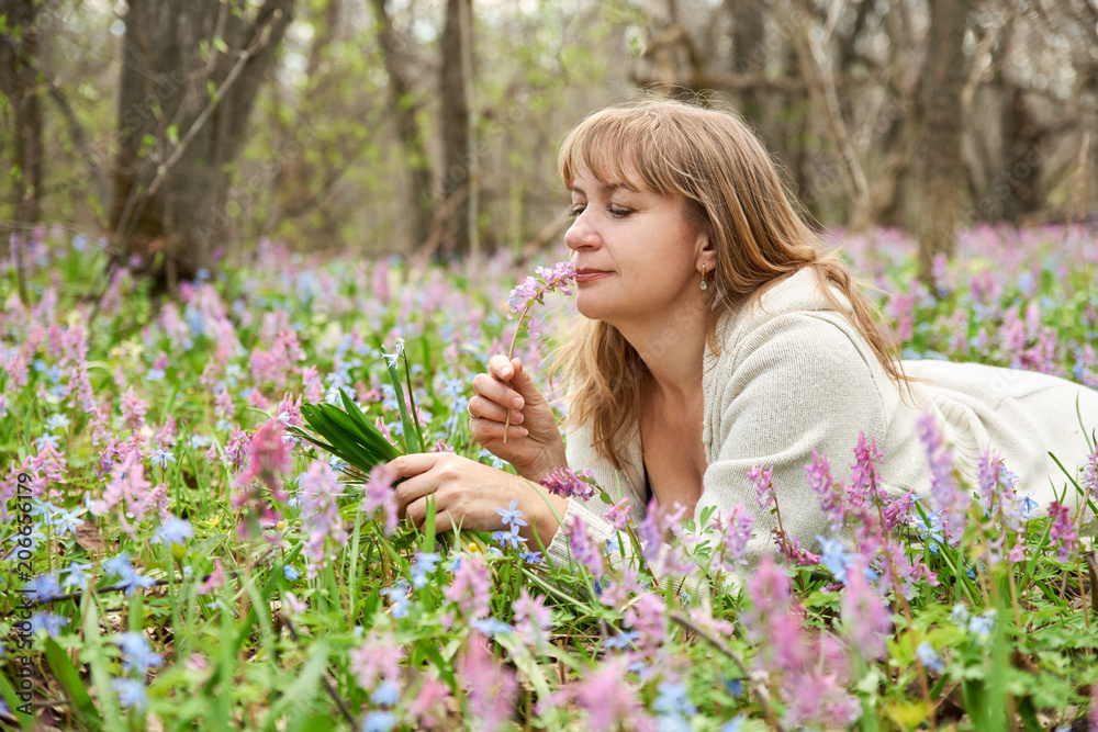 A pensive dreamy woman looks at a bouquet of flowers in her hands lying in a meadow with flowering forest grass A pensive dreamy woman looks at a bouquet of flowers in her hands lying in a meadow with flowering forest grass