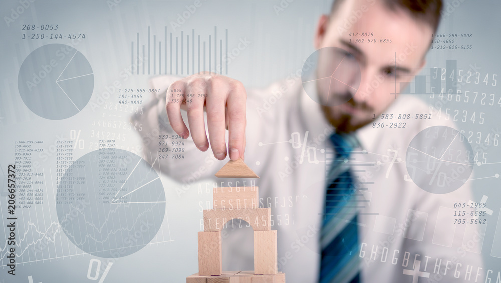 Obraz premium Young handsome businessman using wooden building blocks with data and numbers around him