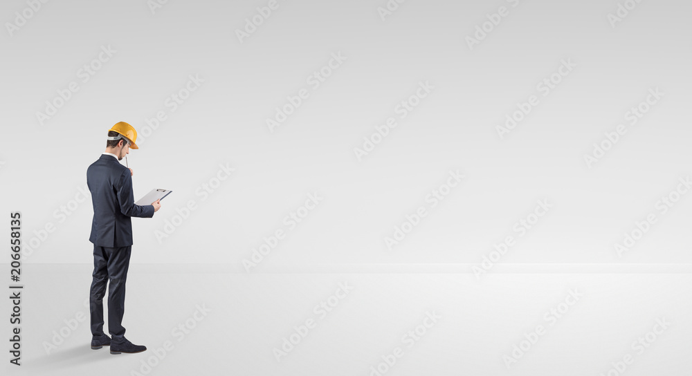 Young architect with construction helmet standing in an empty space and holding a plan

