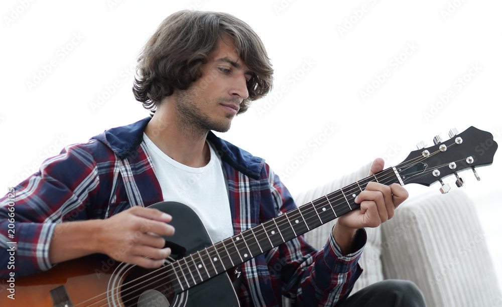 Fototapeta premium Handsome man playing on the guitar on the couch at home