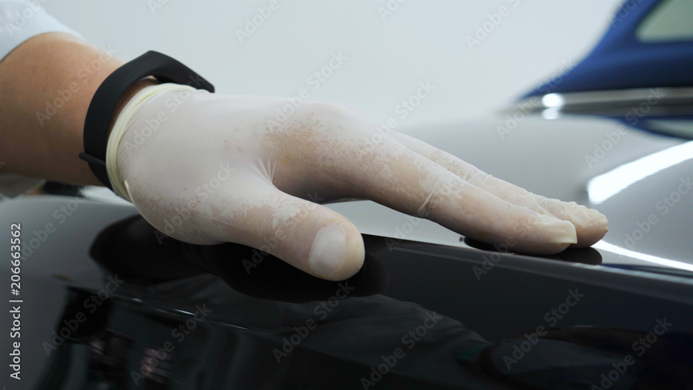 Professional master after polishing and painting cars, checks scratches, white rubber gloves, white coat, goggles, auto service