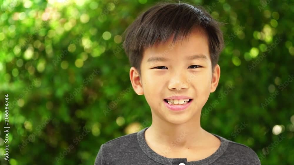 Slow motion zoom out of young Asian Thai boy smiling in a garden Slow motion zoom out of young Asian Thai boy smiling in a garden