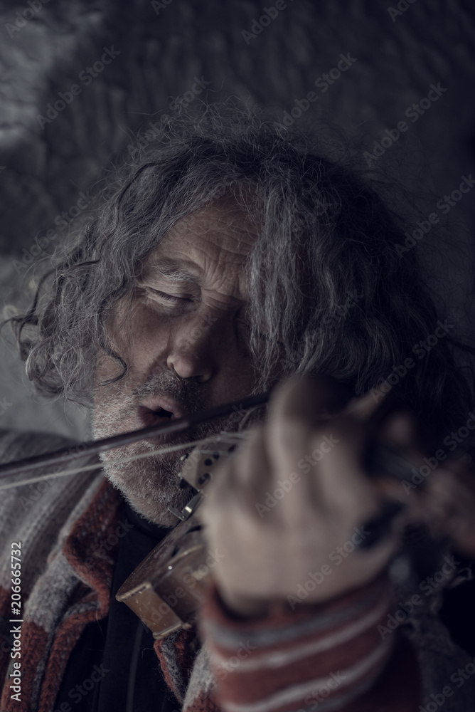 Retro toned image of  man with gray hair and beard singing as he plays a violin