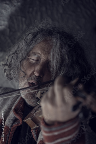 Retro toned image of man with gray hair and beard singing as he plays a violin