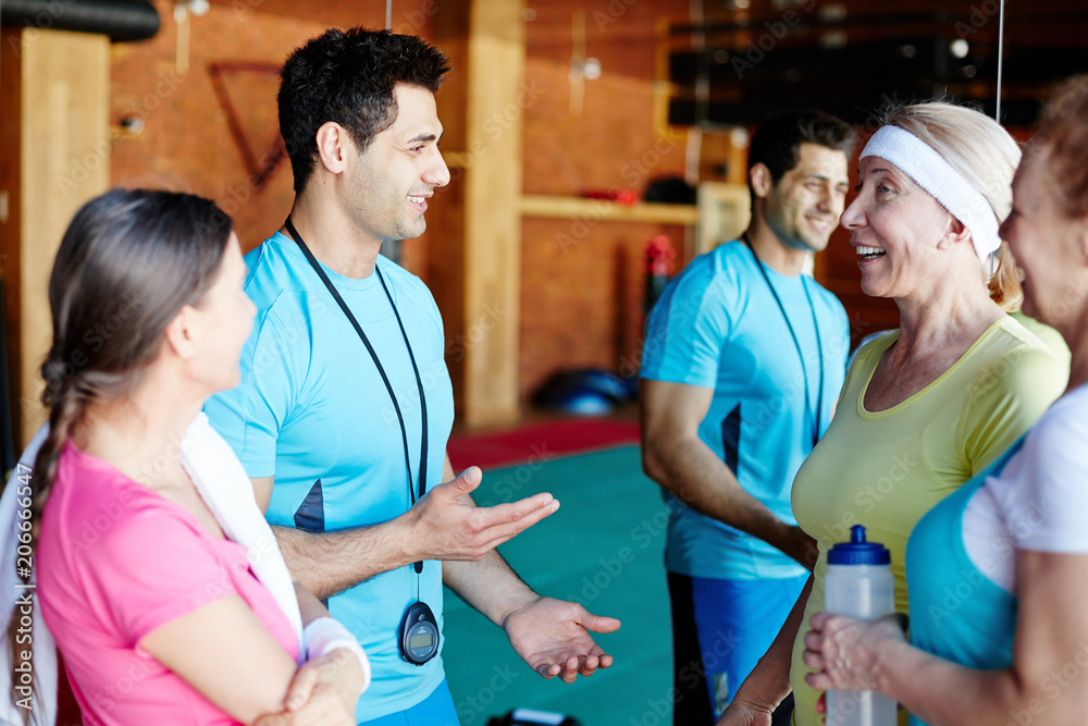 Young coach and his team standing by mirror in gym and discussing new exercises after training Young coach and his team standing by mirror in gym and discussing new exercises after training