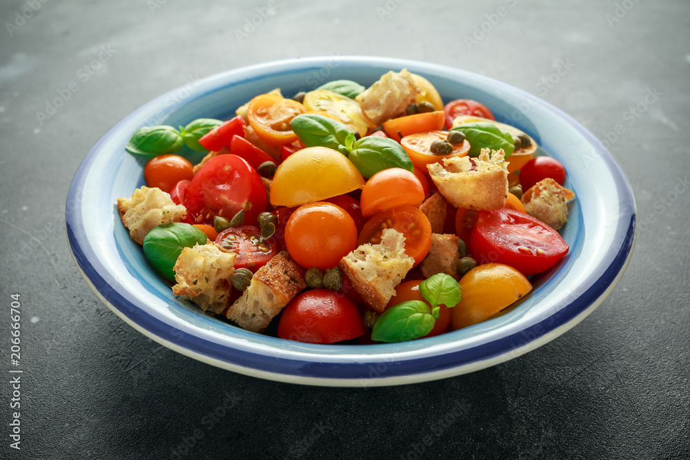 Panzanella Tomato salad with red, yellow, orange cherry tomatoes, capers, basil and ciabatta croutons. summer healthy food.