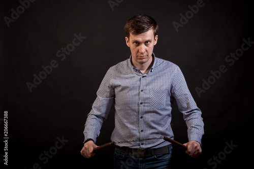 Dark-haired man in a plaid shirt .holds a nunchuck in his hands .on black isolated background