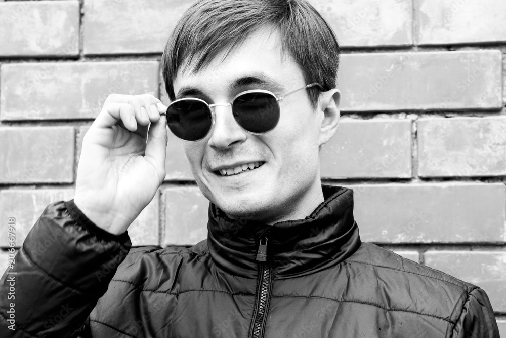 a young man stands leaning against a brick wall adjusts her sunglasses black and white image a young man stands leaning against a brick wall adjusts her sunglasses black and white image
