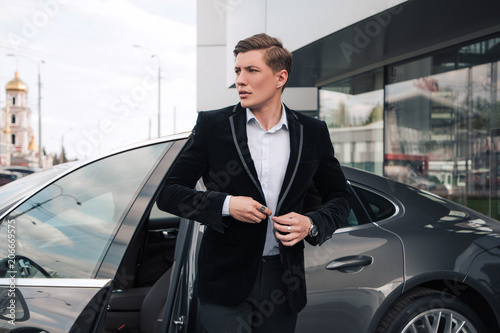Come in time! Handsome serious young entrepreneur buttoning his understated jacket, while going out of his modern car. © stacestock