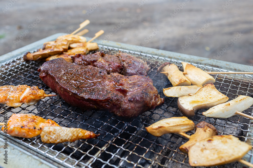Red raw beef steak is placed on grilled grid over charcoal with fire to make it be cooked well and ready to serve as main dish for family’s dinner.