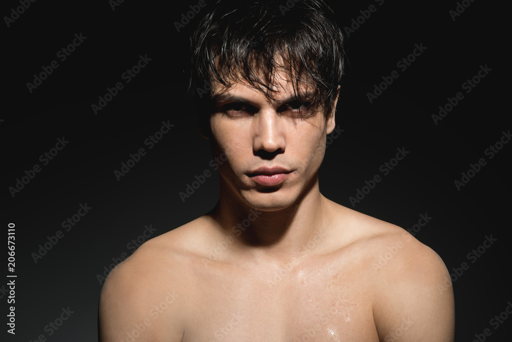 Determination. Portrait of serious young naked man with wet hair is looking at camera confidently. He is standing against dark background. Masculine beauty concept Determination. Portrait of serious young naked man with wet hair is looking at camera confidently. He is standing against dark background. Masculine beauty concept