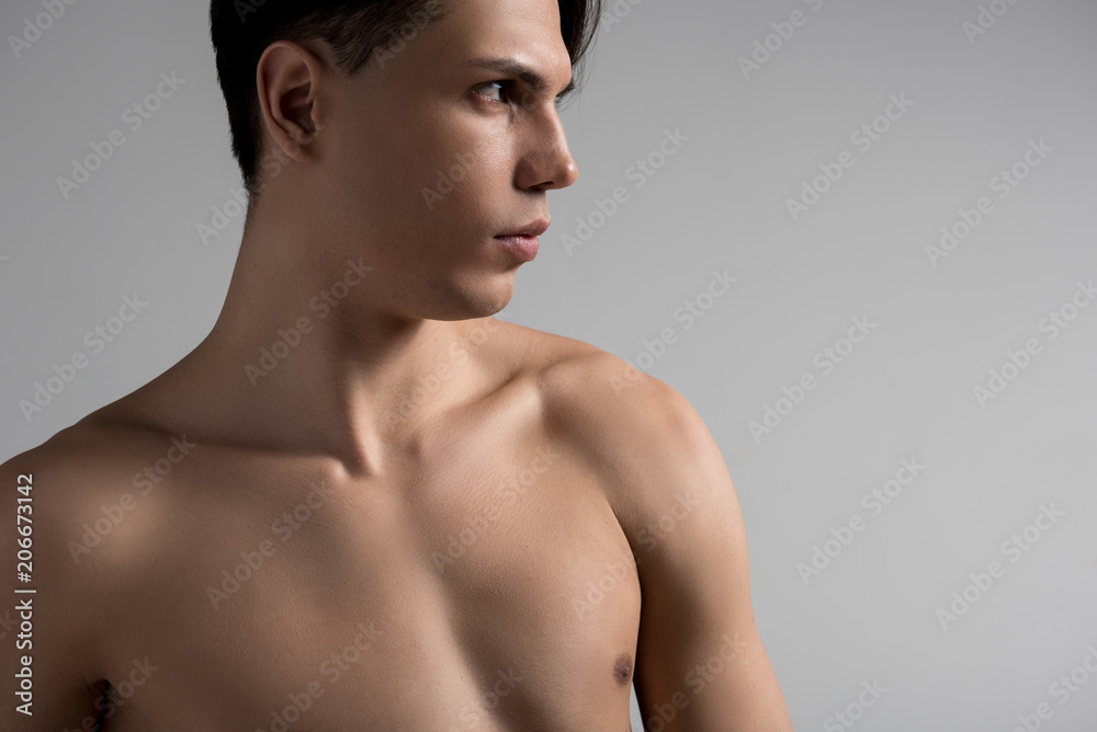 Profile of young gorgeous shirtless guy is standing and expressing  confidence. He is looking aside thoughtfully while demonstrating his perfect  body. Beauty skin concept. Copy space in the right side Stock Photo