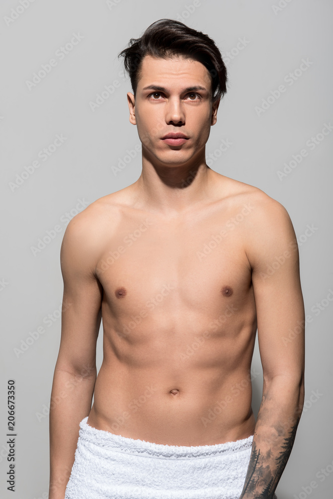 Portrait of pleasant attractive shirtless teenager is standing and demonstrating his perfect and healthy body. He is looking forward thoughtfully with white towel on his hips. Hale and hearty concept