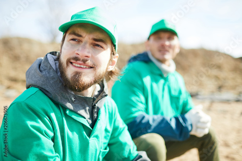 Cuadro en lienzo Bearded guy in green uniform and his colleague having rest after work in natural
