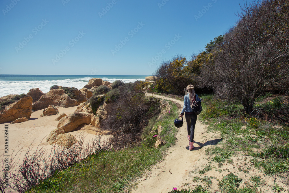 Woman holding helmet for motorcycle travel walking on ocean beach. Algarve, Portugal