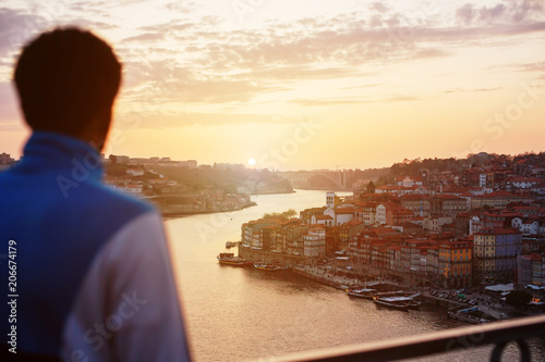 Young african traveler man meets sunset standing on the view point in front of Douro river and Dom Luis I bridge in Porto, Portugal