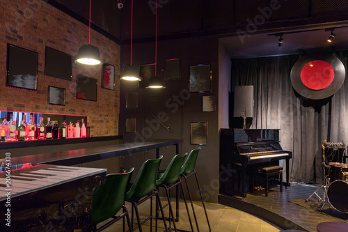Modern jazz bar interior design, stage with black piano, lamps above bar counter © Annatamila