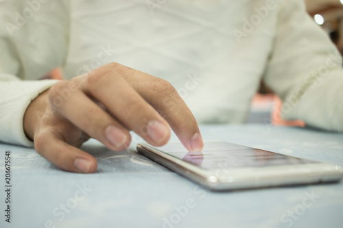 Online searching social networks by Smartphone Concept: Hand of young man pointing finger on blank screen smart phone, using hand clean gadget or typing sms message to his friends on table background