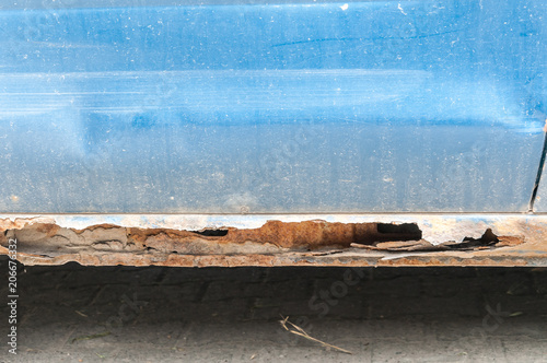 Damaged blue car metal body and scratched paint with rusty corroded parts and hole on the bottom ready for bodywork
