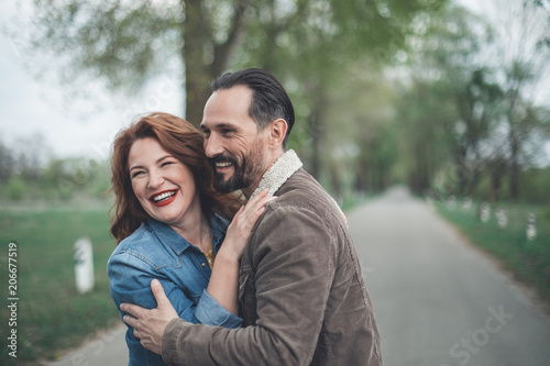 Waist up portrait of glad mature loving couple enjoying date in the nature. They are cuddling and smiling with happiness 