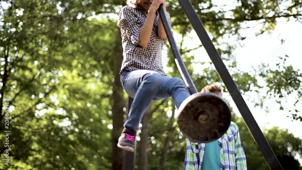 Children having fun is riding zipline. Cute girl and teen boy moving on zip line at playground - outdoors.