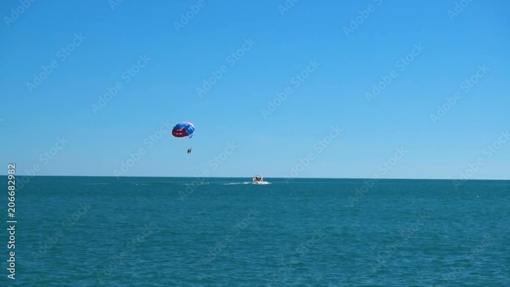 a colored parachute hovers in the sky attached to the boat. in the open sea against the blue sky in good weather. sea parasailing a colored parachute hovers in the sky attached to the boat. in the open sea against the blue sky in good weather. sea parasailing