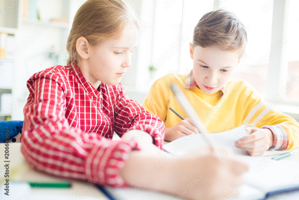 Two diligents classmates looking in manual and making notes in their copybooks at lesson Two diligents classmates looking in manual and making notes in their copybooks at lesson