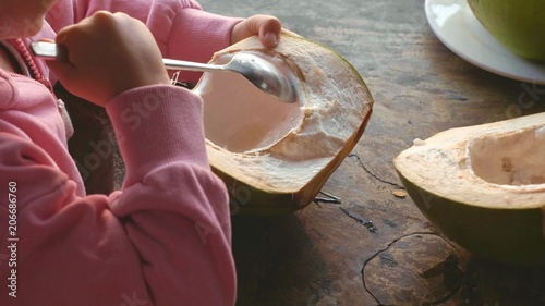 Little cute girl eating coconut by spoon at cafe